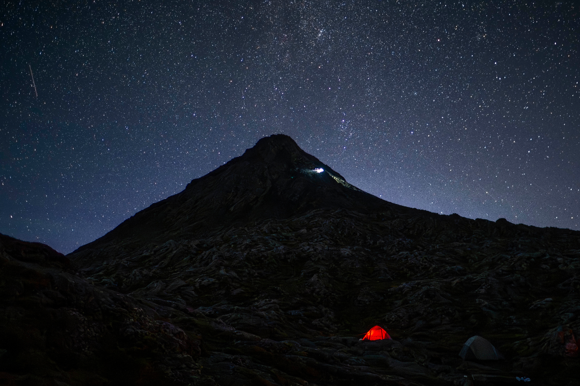 Mount Pico under a starry night sky with a lit tent at base camp